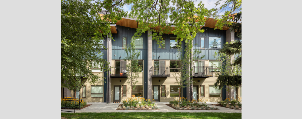 The front façade of four 3-story townhouses, with landscaping and mature trees in the foreground.