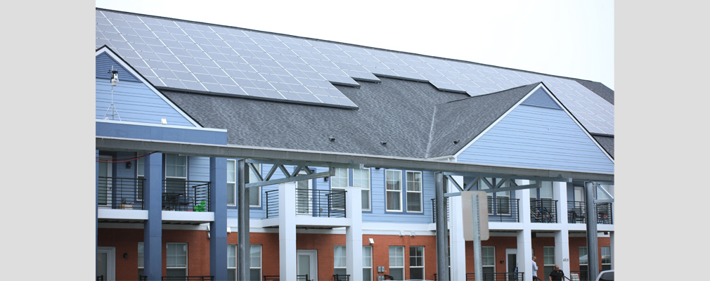 Photograph of the front façade of an apartment building, with roof-mounted solar panels.