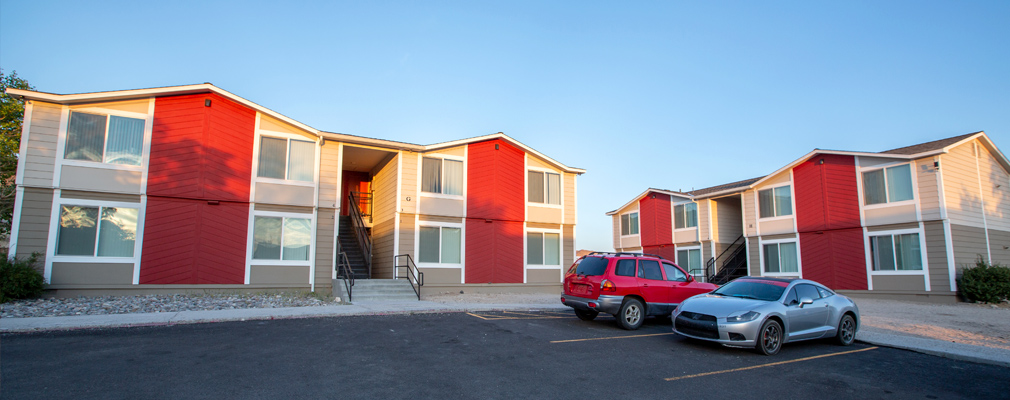 Two 2-story walkup apartment buildings, with two cars in a parking lot in foreground.