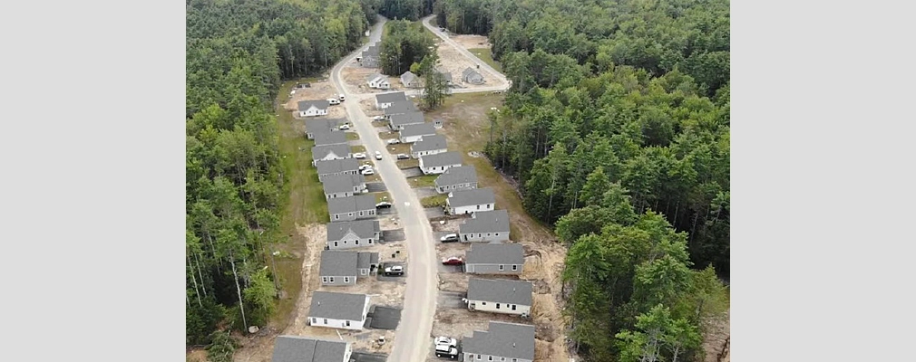 A street in a wooded area lined with small, single-family homes on both sides. 
