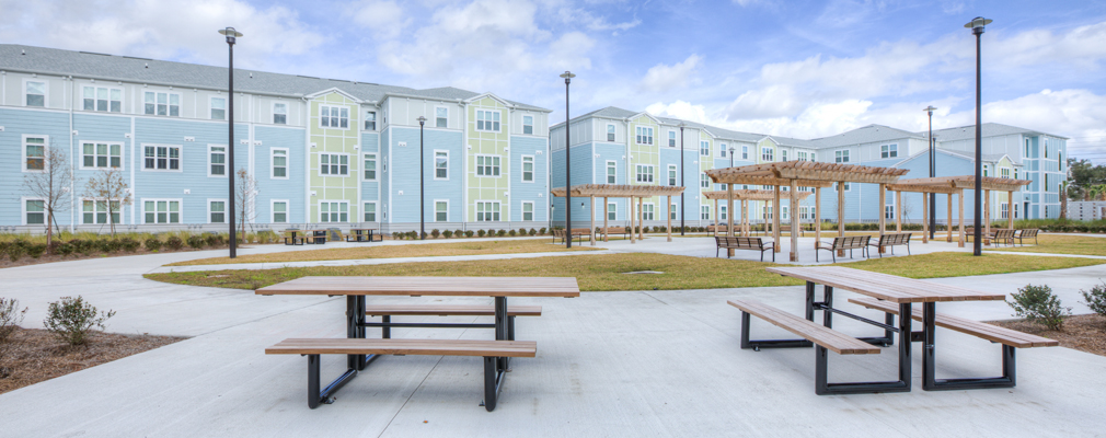 Picnic tables, benches, and pergolas in a large courtyard with a three-story apartment building in the background.