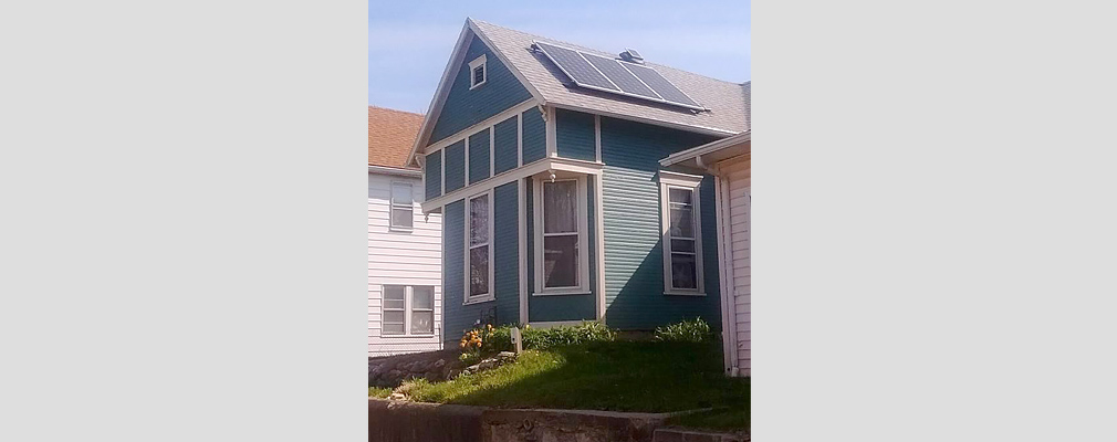 Photograph of the front façade of one-story, clapboard house between two small houses on lots elevated several feet above the sidewalk.