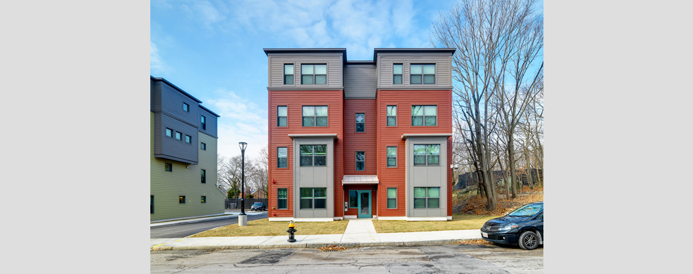 Four-story, red and gray residential building with road and sidewalk in front.