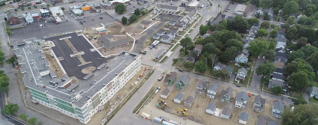 Low-angle aerial photograph of the Eastman Reserve, including newly constructed single-family detached houses with rear-yard garages (bottom right and top center) across the street from older single-family houses (on wooded lots).