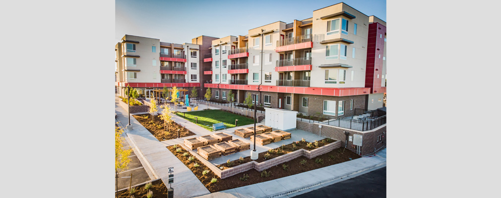 Four-story residential building with balconies and a landscaped courtyard in the foreground.