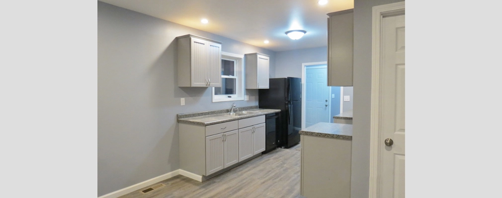 Modern kitchen with gray flooring, blue-gray walls, and a doorway opening into another room.