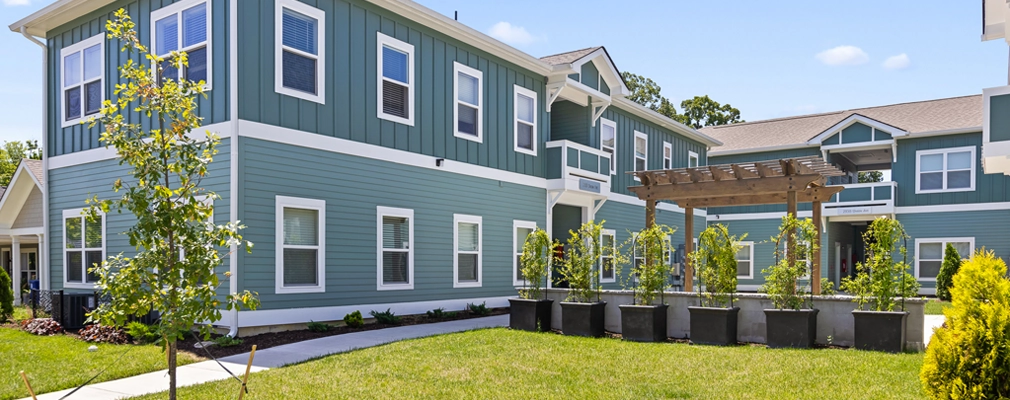 Photograph of 2 two-story apartment buildings facing a landscaped courtyard with a wooden pergola structure and a row of planter boxes.