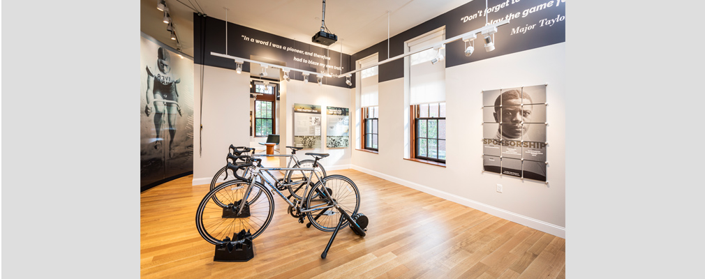 Photograph of the interior of the Major Taylor Museum on the site of Courthouse Lofts with displayed exhibits on the walls in the background and bicycles in the foreground.