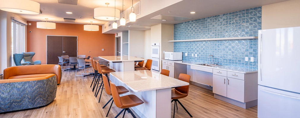 An interior photograph of a kitchen with an island and seating in the foreground and chairs, tables, and sofas in the background.