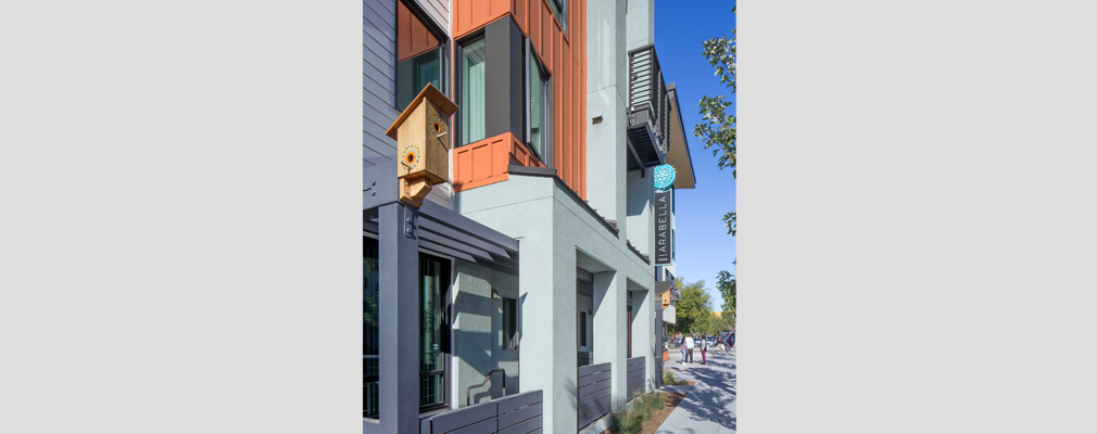 Photograph of the lower floors of a multifamily building with three porches, a balcony, and a birdhouse as well as a sign on the second level that reads "CASA ARABELLA."