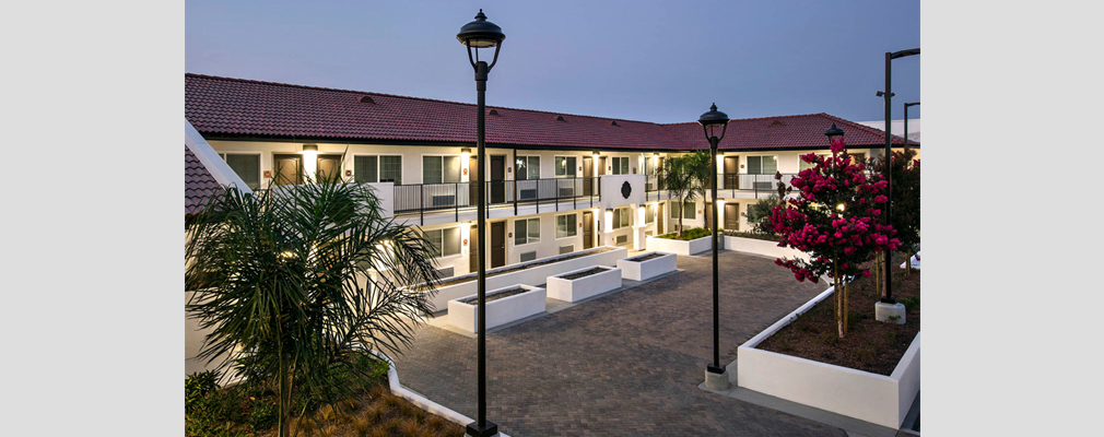 Low-aerial photograph of the interior courtyard at dusk, with a two-story walk-up apartment building in the background.