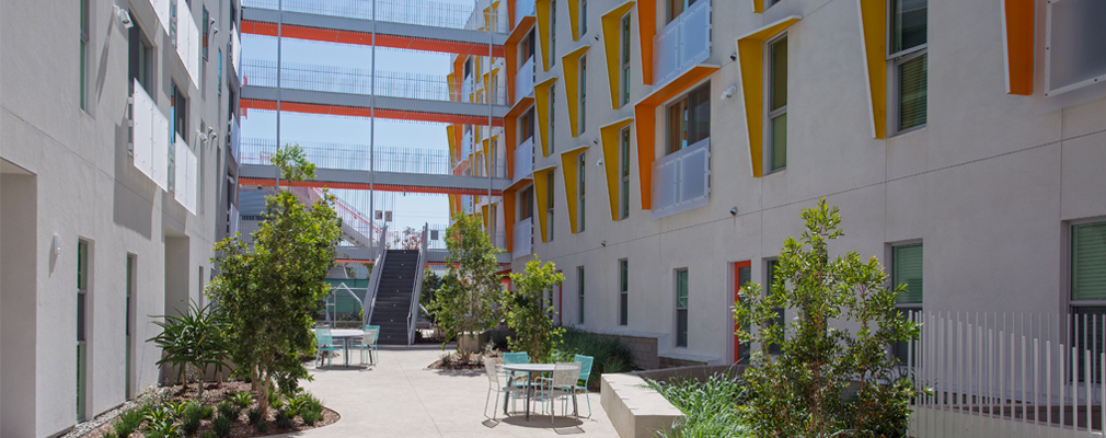 Photograph of landscaped courtyard framed by a walkway joining two wings of a five-story residential building.