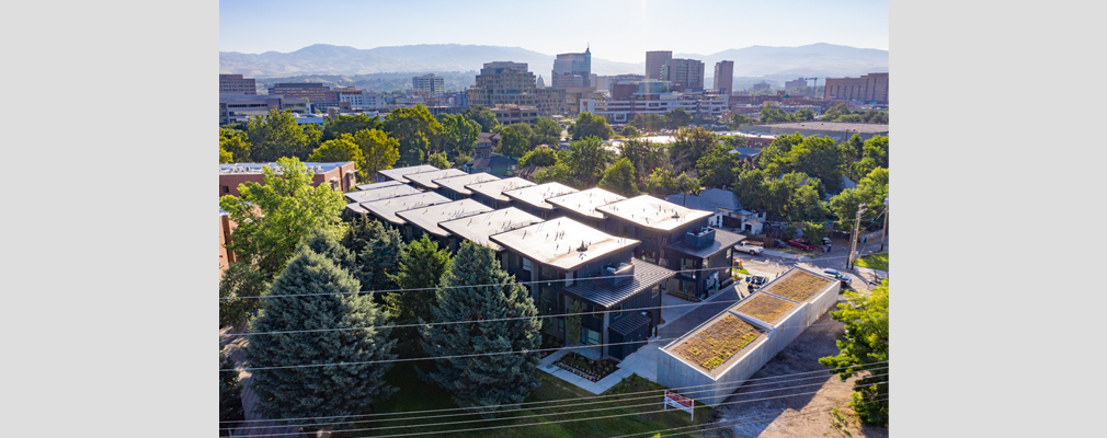 Two 3-story townhouse buildings and a parking structure with a green roof against the backdrop of the downtown skyline and mountains.