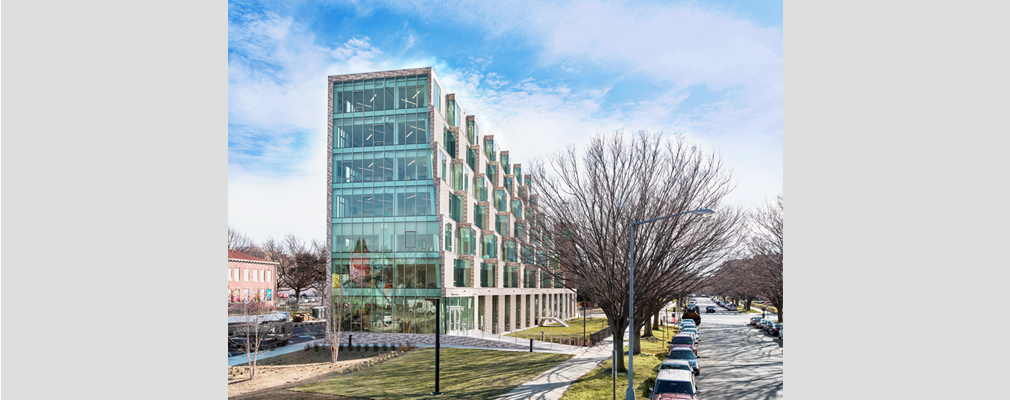 Ziggurat-shaped residential building next to a street with parked cars.