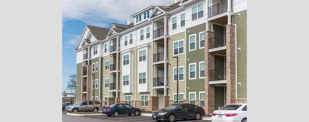 Ground-level view of a four-story apartment building with parked cars.