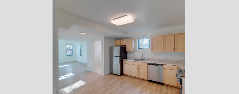 Kitchen and an unfurnished room in an apartment with sunny windows.