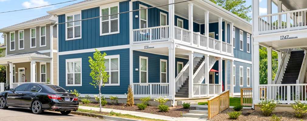 A photograph of 2 two-story quadplex buildings with covered staircases and upper and lower porches, with a landscaped sidewalk and street in the foreground.