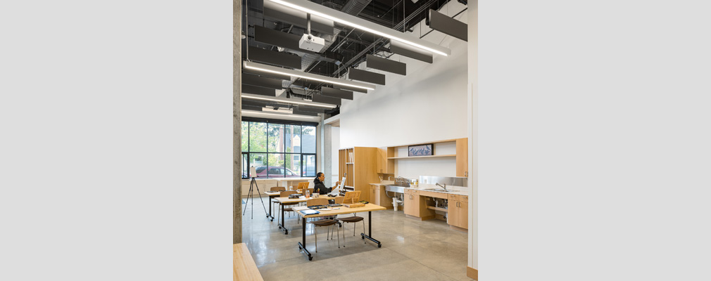 An interior photograph of a room with three movable tables and chairs, cabinet and shelving on the right, and windows in the background.