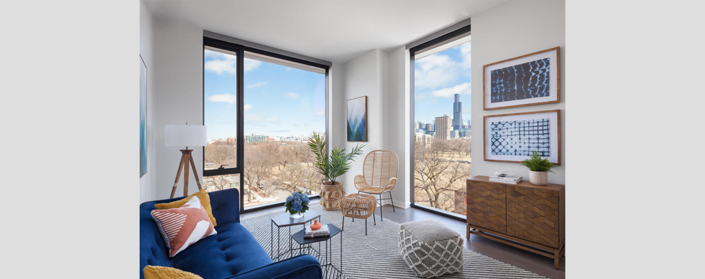 Photograph of a living room, with floor-to-ceiling windows set in two walls, one of which reveals the skyline of downtown Chicago.