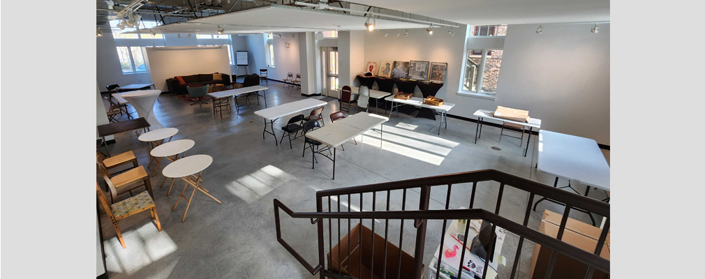 Large room with tables, chairs, and artwork along a wall.