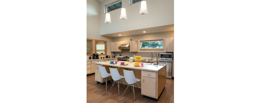 A kitchen with an island in the foreground with three chairs and settings for breakfast.