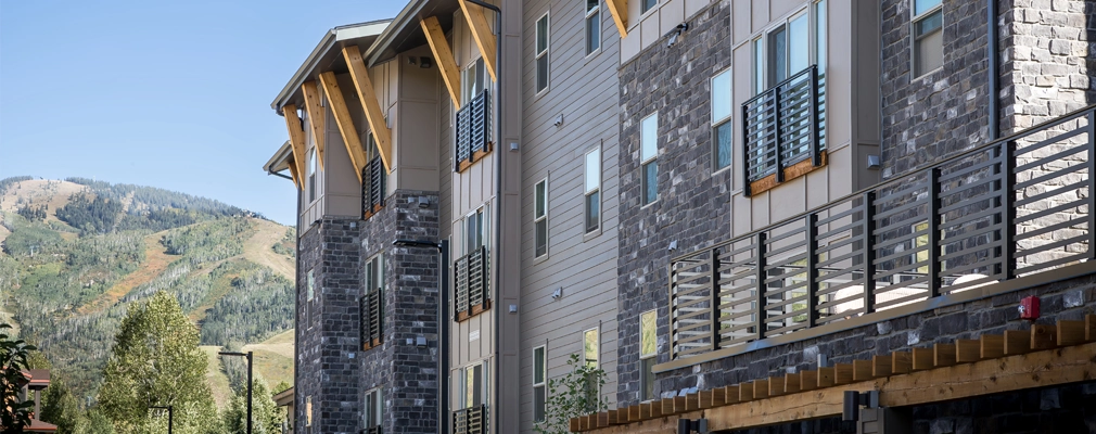 An exterior view of a four-story building with small balconies and mountains visible in the background.