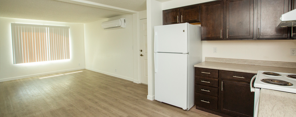 A kitchen with upper and lower cabinets and an unfurnished living area.