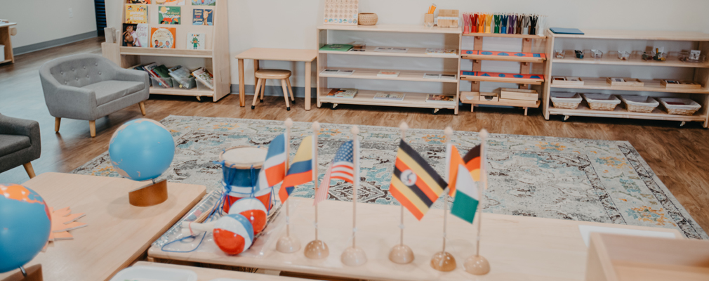  A preschool classroom with bookshelves along a wall and globes and desktop country flags in the foreground.