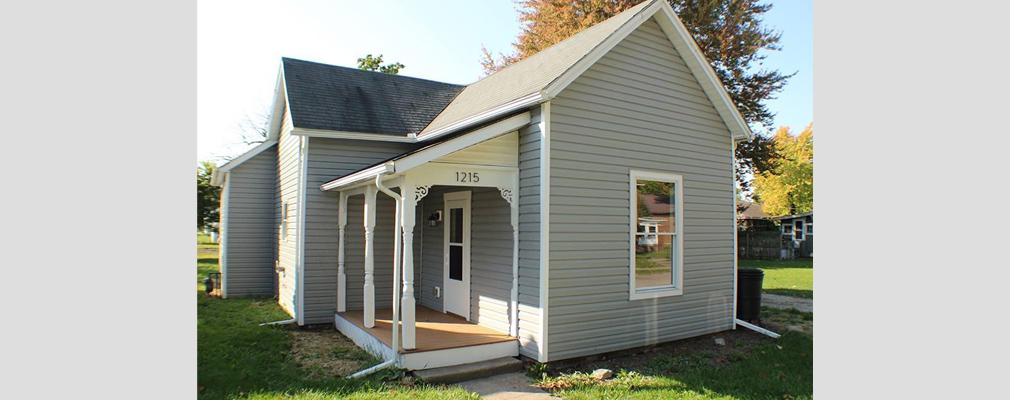 Photograph a of a small, single-story house with a covered side-entrance. 