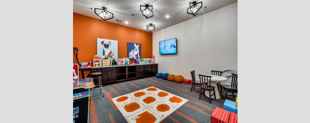 Colorful room with a rug, a table with four chairs, and a cabinet area with bins filled with toys along the back wall.