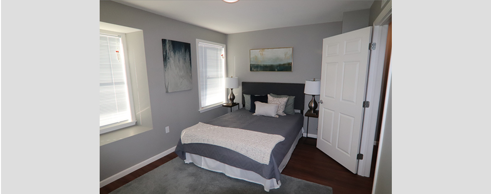 Bedroom with a made-up bed, two night stands with lamps, and carpeting.