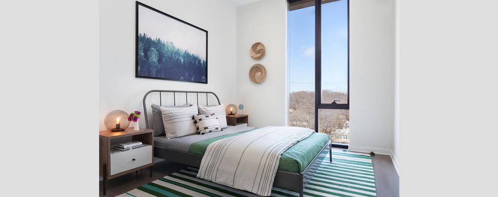 Photograph of an apartment bedroom with a floor-to-ceiling window in one wall.