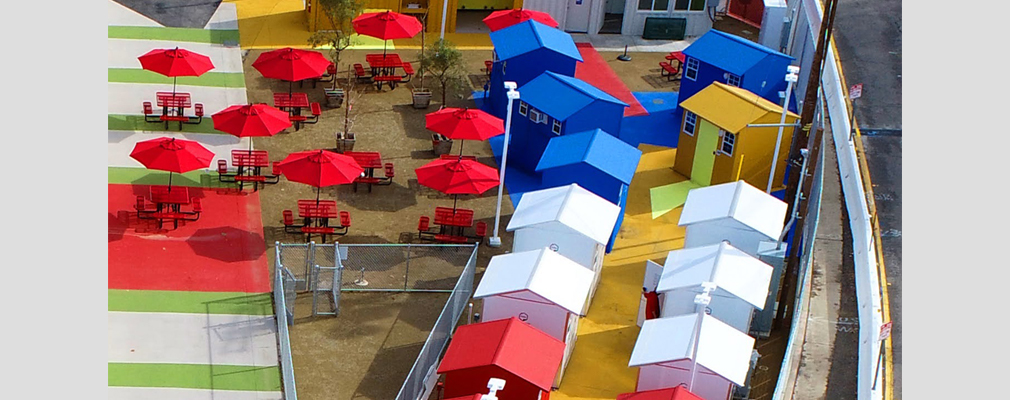 Aerial photo of a group of tiny homes, a cluster of red outdoor tables, and a fenced area for dogs.