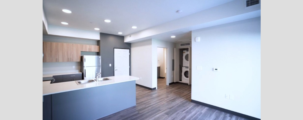 Photograph of a kitchen area in the foreground and a washer and dryer in a closet in the background.