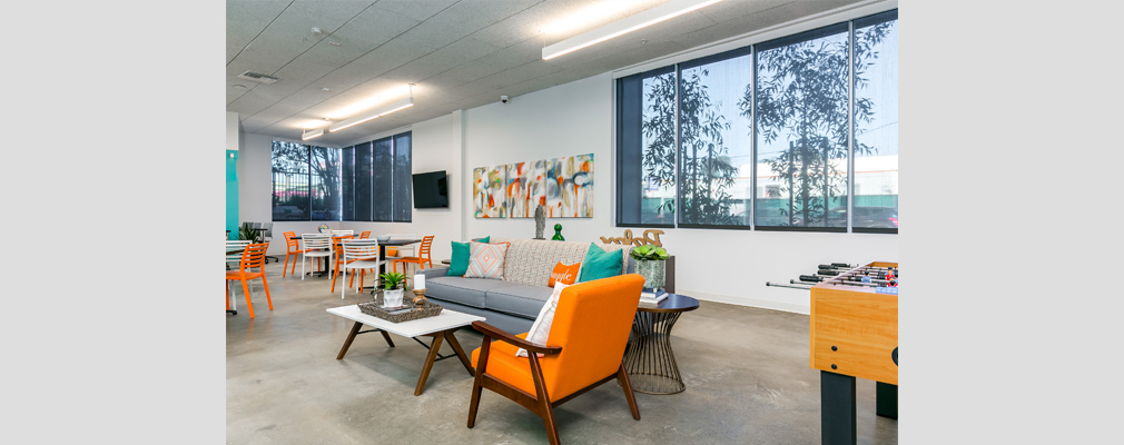 Photograph of a community room featuring seating arranged around tables, a television, and a foosball table.