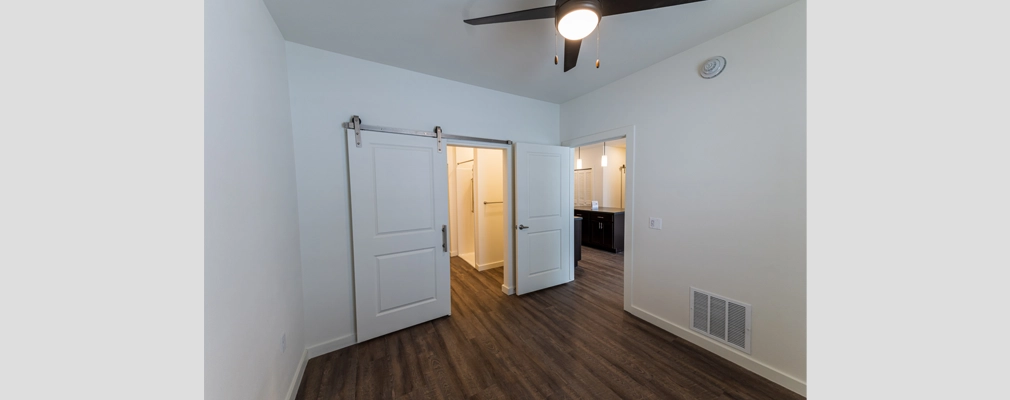 An interior view of a bedroom with a ceiling fan and doors leading to a bathroom.