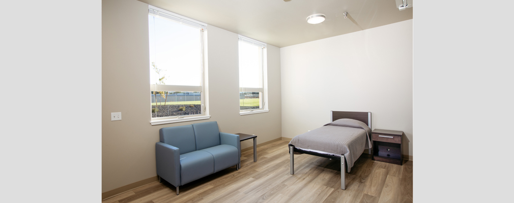 Photograph of the interior of a bedroom at Chuck Austin Place with a bed, nightstand, and small couch.