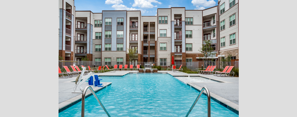 A resort-style pool with pool chairs situated in the interior courtyard of a four-story building.