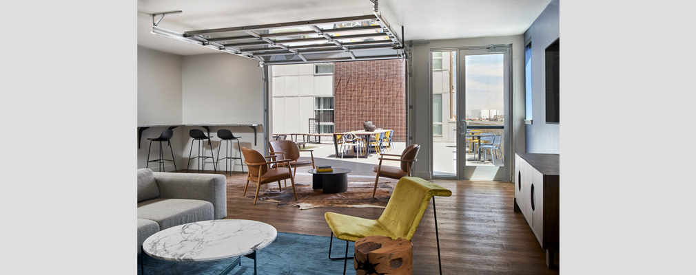 Photograph of a large room with several chairs and tables and a rear wall that opens to a second-story outdoor common space.  