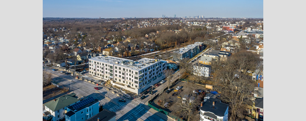 Aerial view of residential neighborhood with an apartment building in the foreground and the Boston skyline in the distance. 