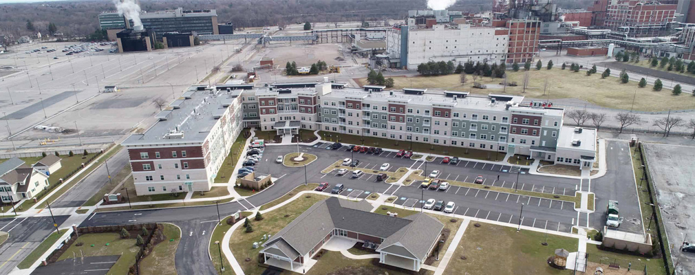 Low-angle aerial photograph of a multifamily building, with several industrial buildings in the background.