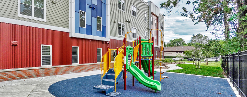 Photograph of a play structure next to a three-story apartment building.