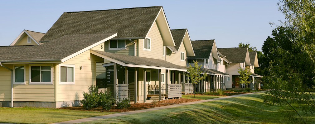 An angled view of a row of two-story townhomes with green space and trees in the foreground.