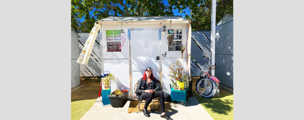 A woman sitting in front of a decorated tiny home. 