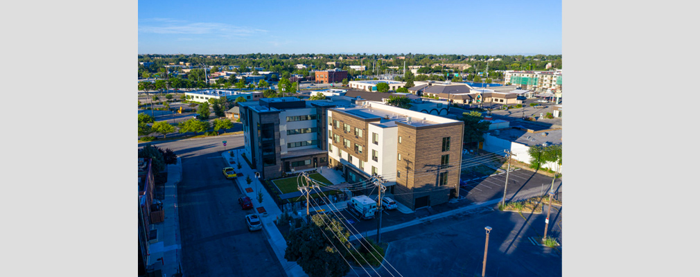 Low-angled aerial photograph of the rear of a multistory residential building and surrounding streets and buildings.