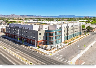 Low aerial photograph of a four-story building situated at an intersection with a mountain range in the background.