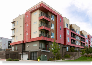 Four-story residential building with balconies on each floor and a side entrance and garage door.