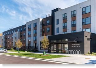 Front façade of a four-story apartment building with the sign "Blooming Meadows" on the wall.