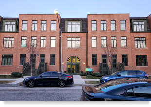 Three-story brick apartment building with cars parked in front.