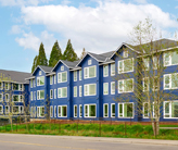 Exterior image of a three-story, L-shaped apartment building painted bright blue with white trim.